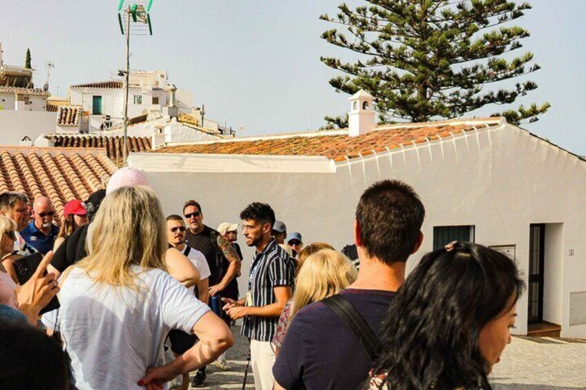 A group of people gathered on a rooftop with a view of a coastal town and a large tree. 5