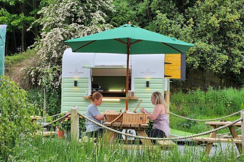 Un carrito de comida móvil con un toldo verde, una mesa de madera y una barrera de cuerda en un área con césped. 2