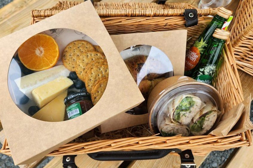 Una cesta de mimbre con alimentos, incluyendo queso, galletas y una botella de cerveza. 3