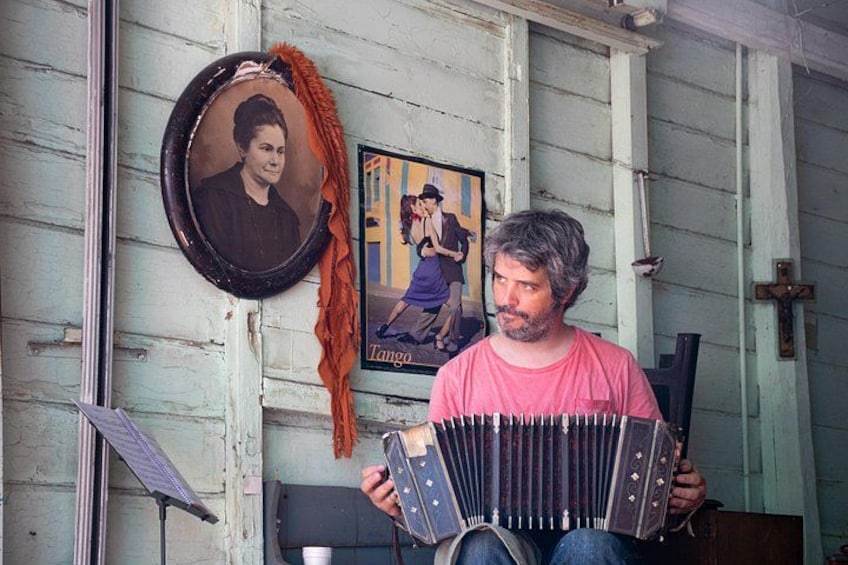 Una persona toca un acordeón en una habitación rústica con un retrato y un cartel en la pared. 1