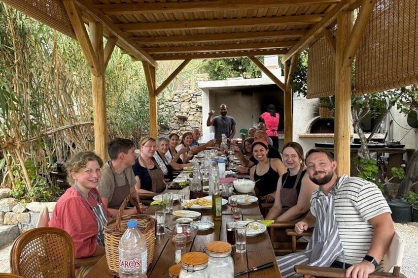 Un grupo de personas cenando al aire libre en una mesa de madera, con cestas y botellas. 3