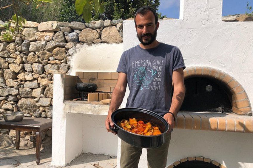 A man holding a pot of food in front of a stone oven. 2