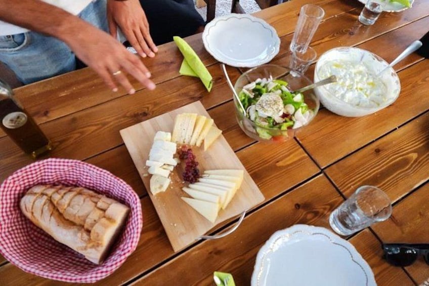 A wooden table with a cheese board, a salad, bread, and a bottle of wine. 5