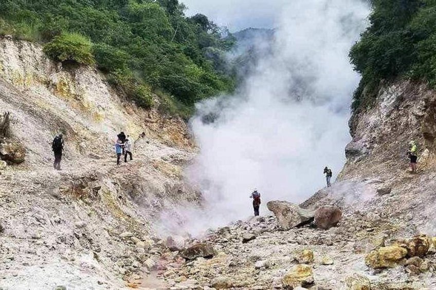 Un paysage volcanique où de la vapeur s’élève du sol, entouré de randonneurs. 2