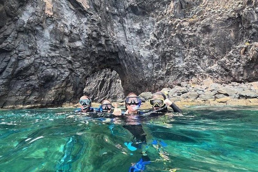 Snorklare i klart vatten med en klippig grotta i bakgrunden. 2