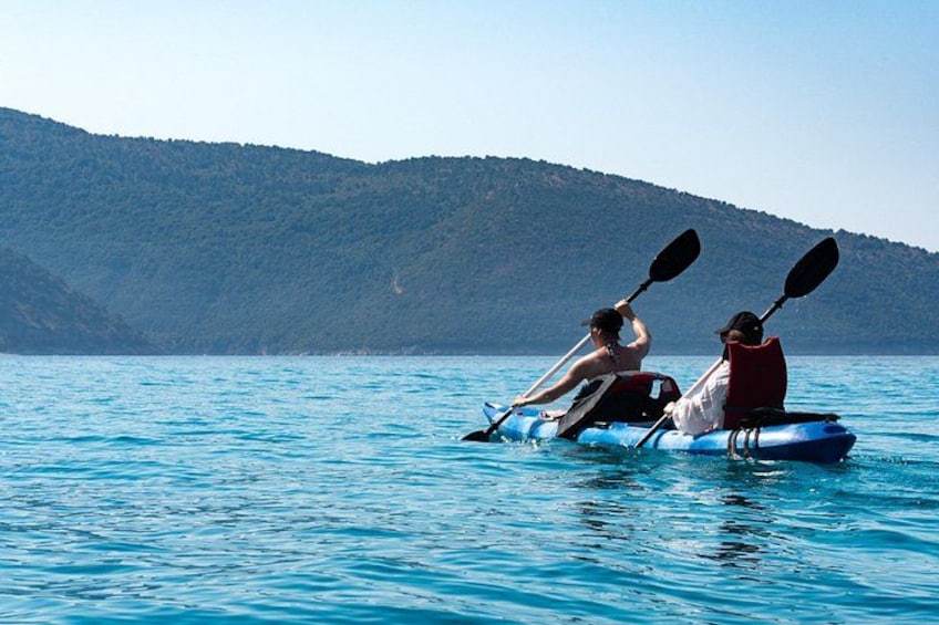 Two people kayaking on a calm body of water with a hilly landscape in the background. 2