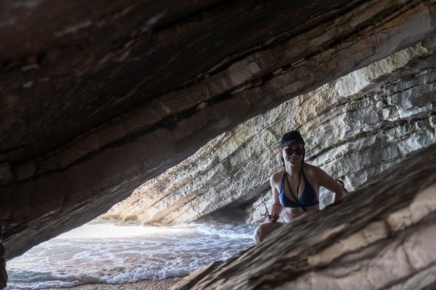 A person in a bikini under a rocky overhang by the sea. 4