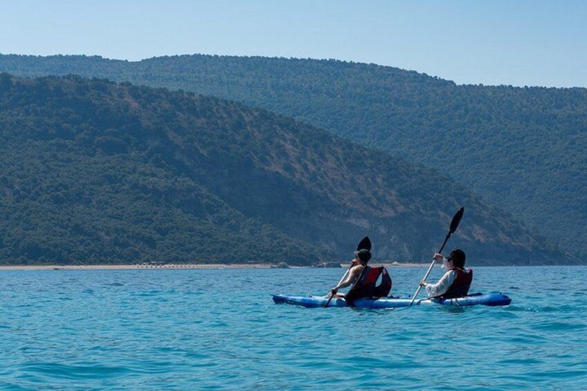Two people kayaking on a calm sea with a forested hill in the background. 5