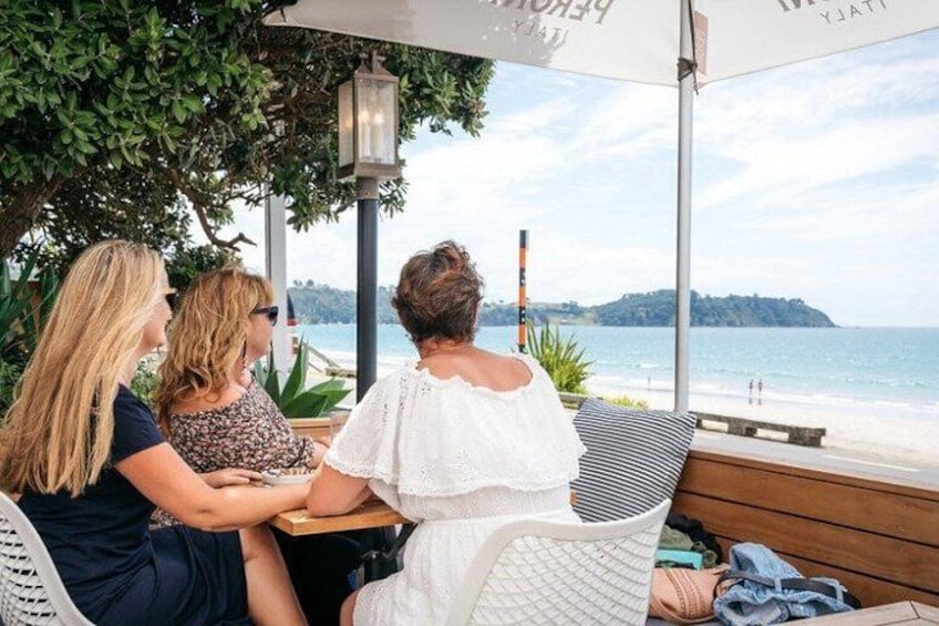 Three people seated at an outdoor table with a view of the beach and ocean. 1