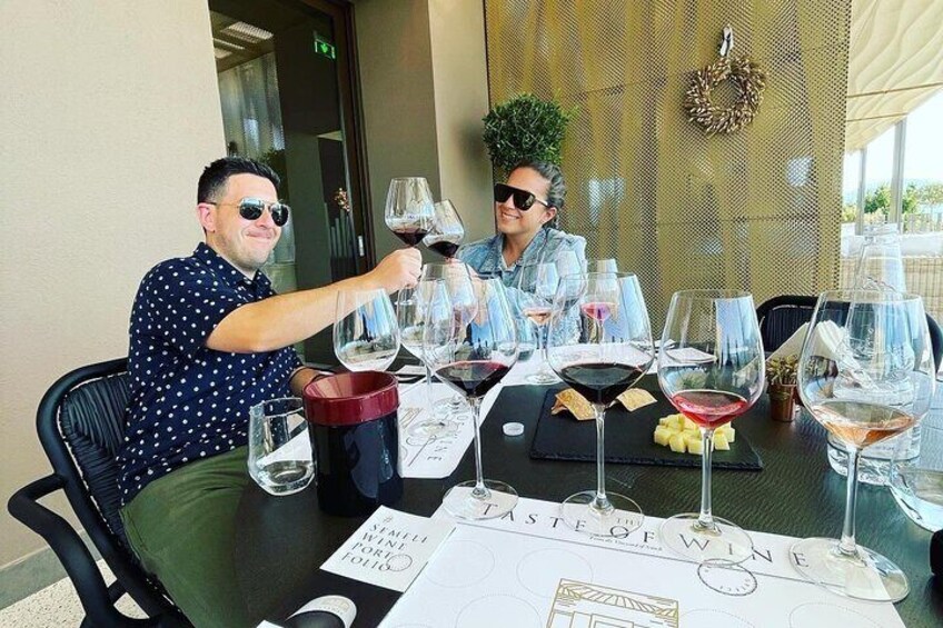 Twee personen zitten aan een tafel met wijnglazen, een menukaart en een placemat met de tekst 'TASTE OF WINE'. 4