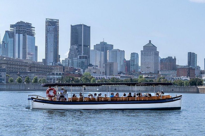 Un barco de paseo fluvial con pasajeros, un horizonte urbano al fondo y un cielo despejado. 4