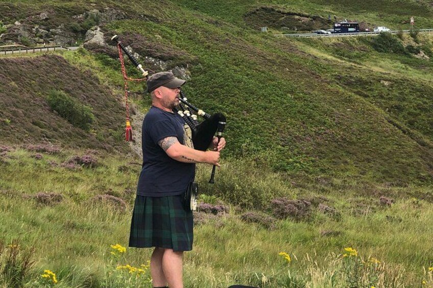 A person playing bagpipes in a grassy field with hills in the background. 3