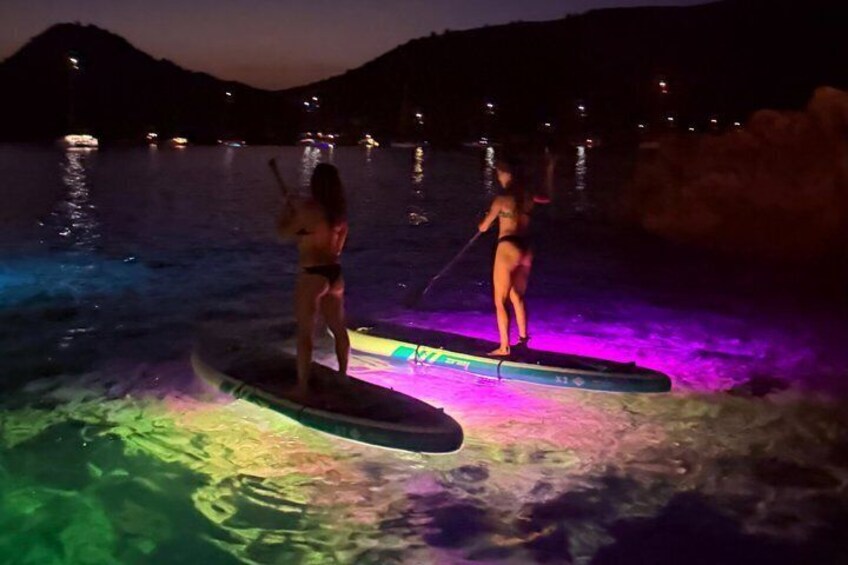 Due persone che fanno paddleboarding su un'acqua illuminata con luci colorate di notte. 2