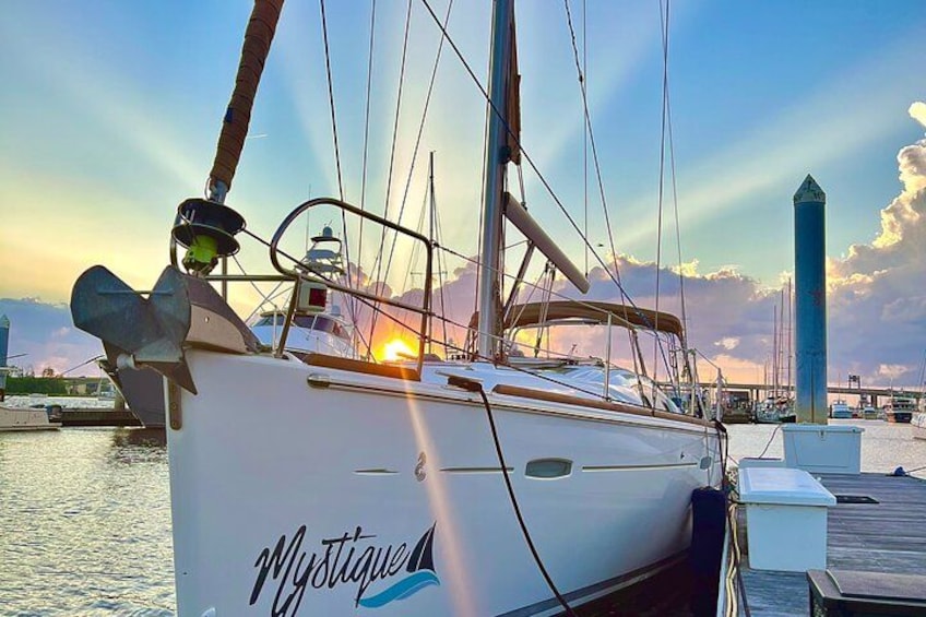 Un velero llamado 'Mystique' amarrado en una marina con un atardecer de fondo. 3