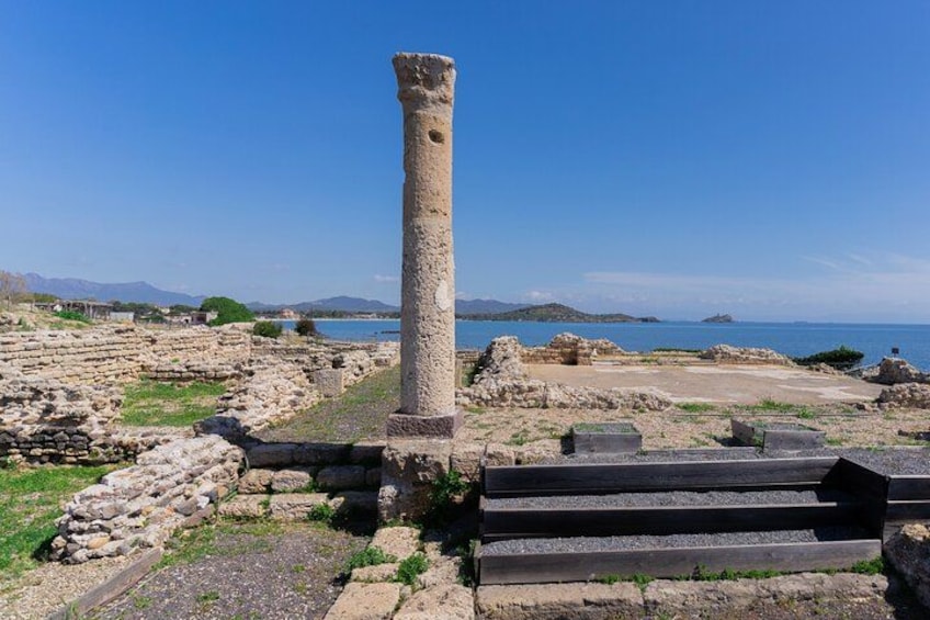 Ancient ruins with stone columns and steps, a clear blue sky, and a distant view of the sea and mountains. 2