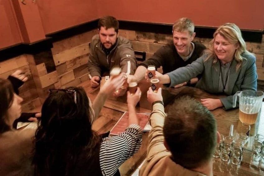A group of people toasting with drinks around a wooden table in a room with brick walls. 4