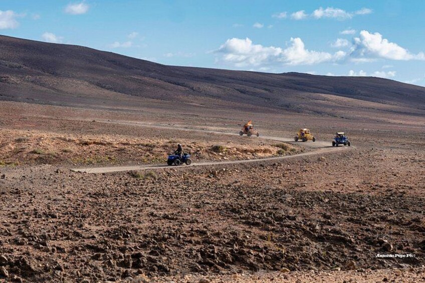 Een kaal landschap met een zandweg, voertuigen en een persoon op een motorfiets. 4