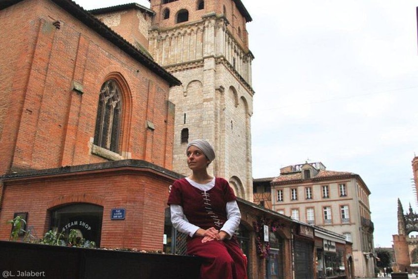 Eine Person in historischer Tracht steht vor einem Backsteinhaus mit einem Turm. 2