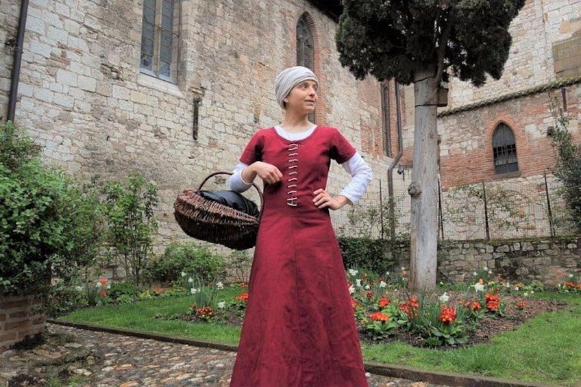 Eine Person in einem roten Kleid steht vor einem Steinhaus mit einem Garten. 1