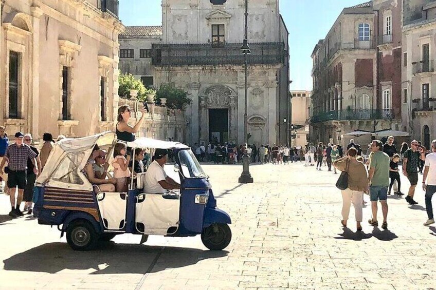 A vintage car with passengers in a cobblestone street. 1