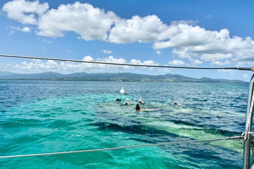 A boat with people swimming in turquoise water, a clear sky, and distant mountains. 5