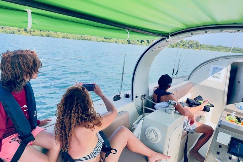 Three people on a boat with a green canopy, water, and greenery in the background. 3