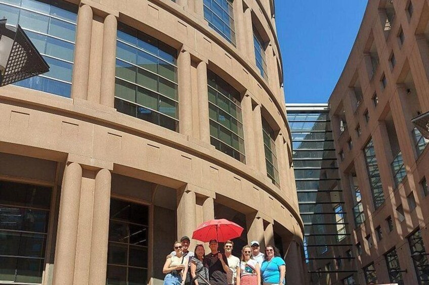 A group of people standing in front of a curved building with large windows and a red umbrella. 2