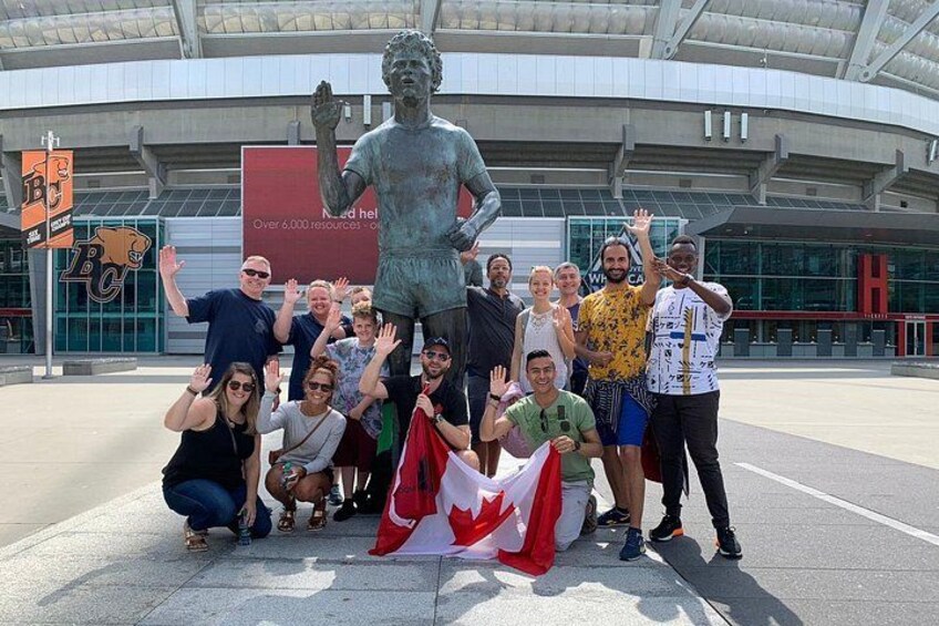 A group of people posing with a statue and a Canadian flag in front of a stadium. 3