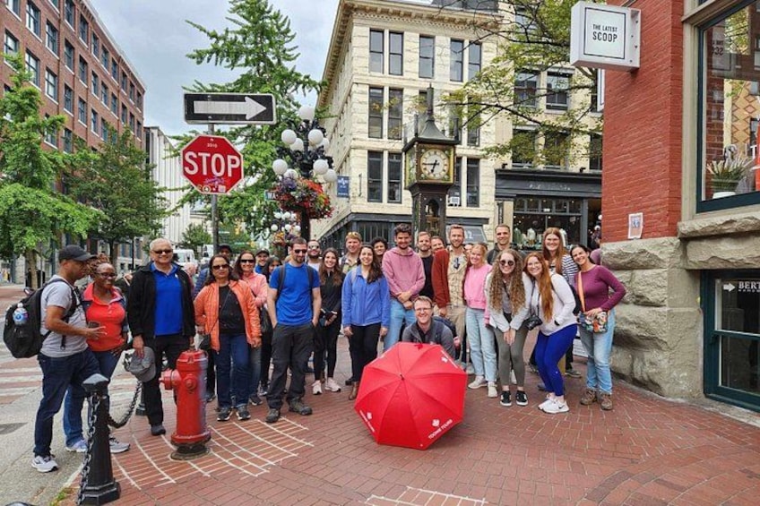 A group of people standing on a brick sidewalk with a stop sign and a red umbrella in the foreground. 1