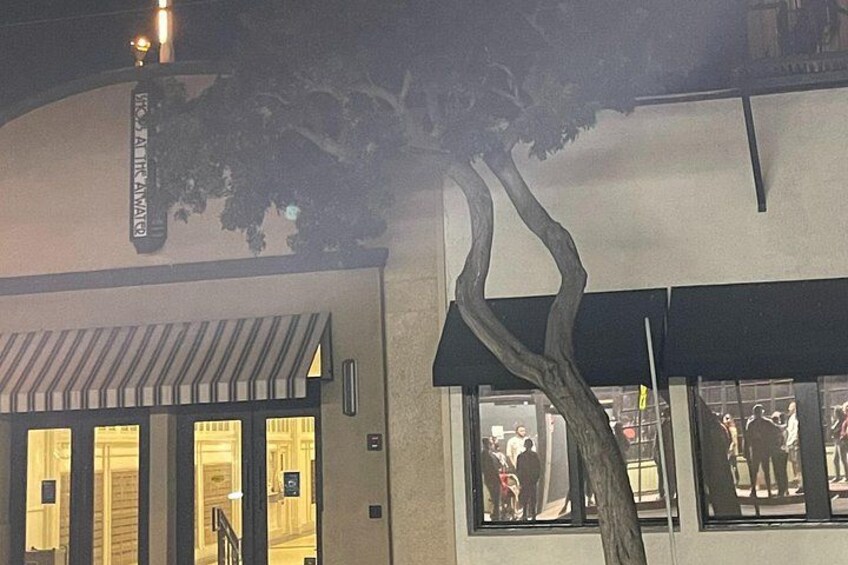 A building with a tree in front, a sign above the entrance, and a storefront with people inside. 4