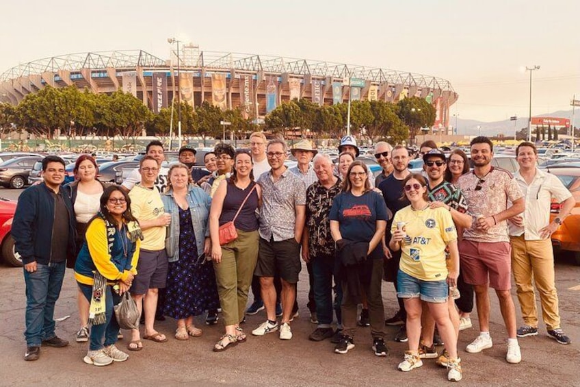 A group of people posing in front of a stadium with a distinctive roof structure. 1