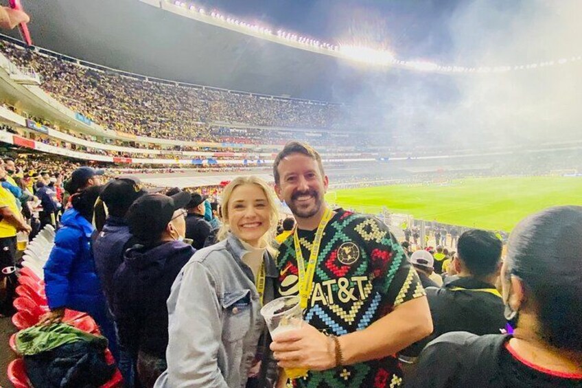 A stadium filled with spectators, a person wearing a colorful shirt with a logo, and another person holding a drink. 2