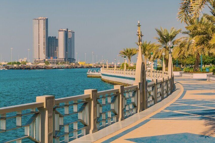 A waterfront promenade with a railing, palm trees, and a city skyline in the background. 4