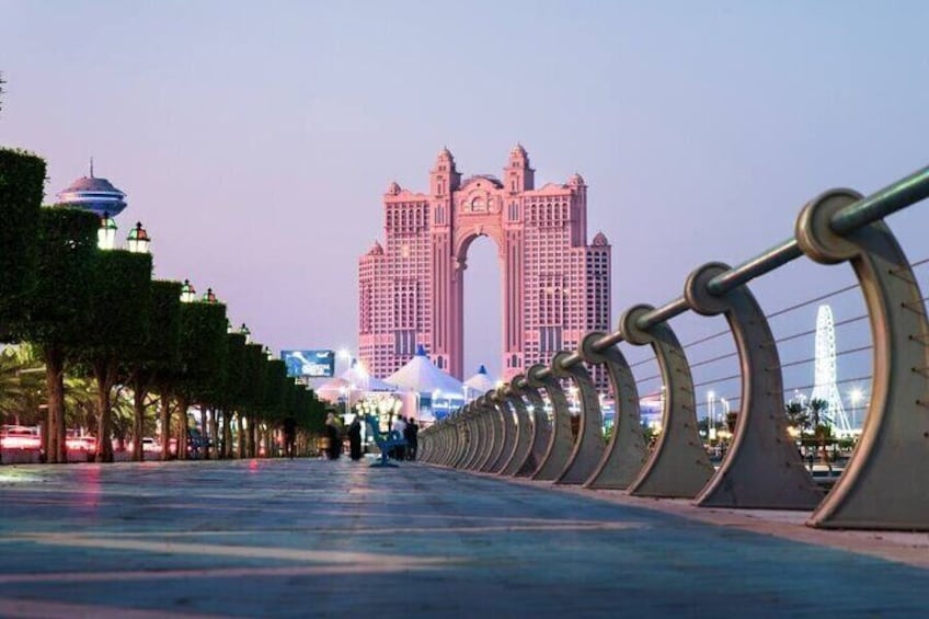 A bridge with a row of lights, a large pink building, and a Ferris wheel in the background. 1