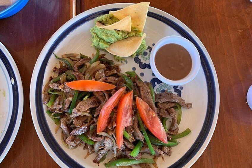 Une assiette de fajitas au bœuf, avec des poivrons et des tomates, une tortilla garnie de guacamole et un petit bol de sauce. 5