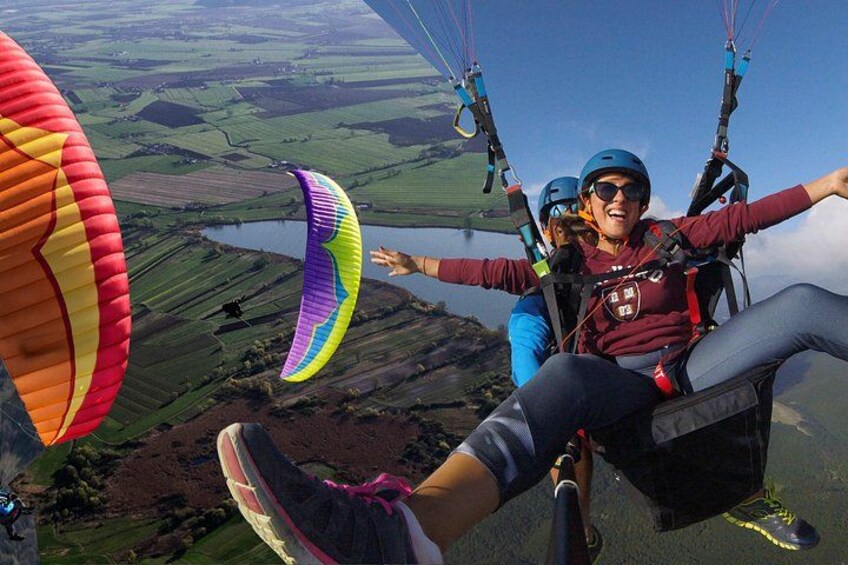 A person paragliding over a landscape with fields and a body of water. 1