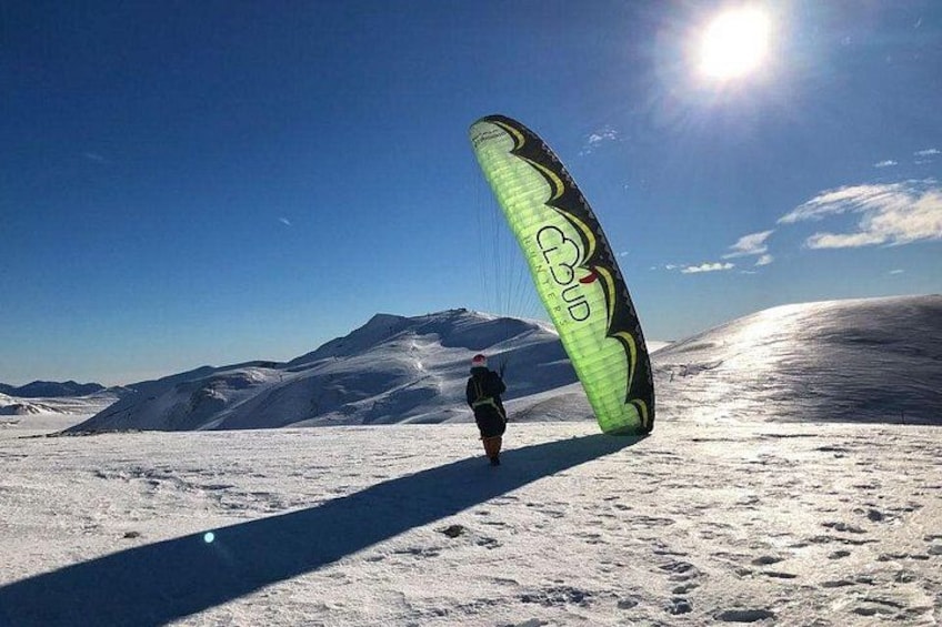 A person with a large kite on a snowy landscape with mountains in the background. 3