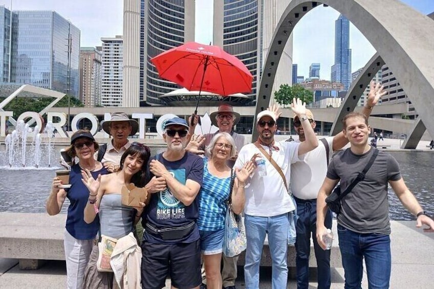 A group of people posing in front of a modern sculpture with the word 'TORONTO' in the background. 1