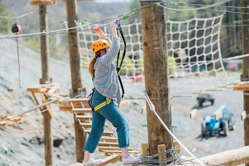 A person on a zip line course with wooden platforms and netted obstacles. 2