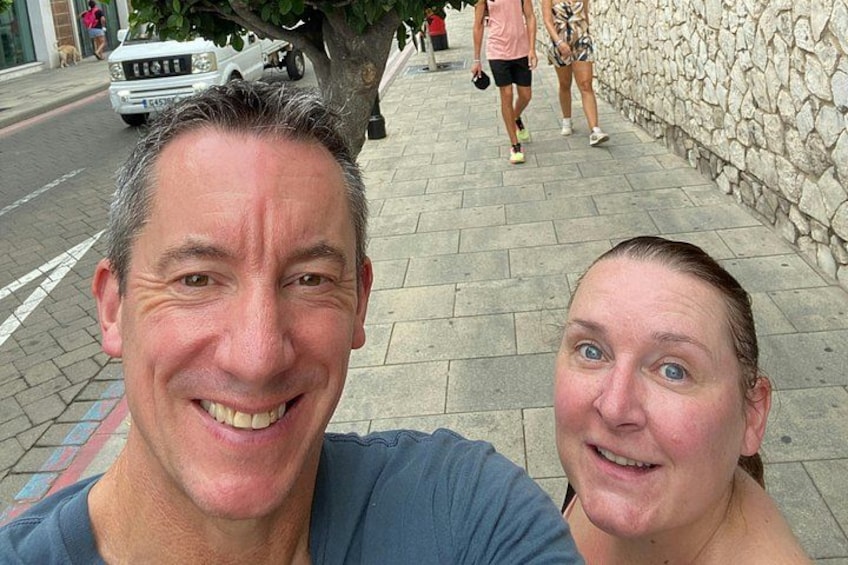 A man and a woman taking a selfie on a sidewalk with a stone wall and a tree in the background. 5