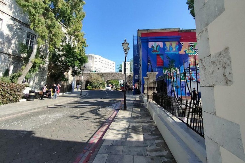 A street with a mural, a building, and a pedestrian walkway. 2