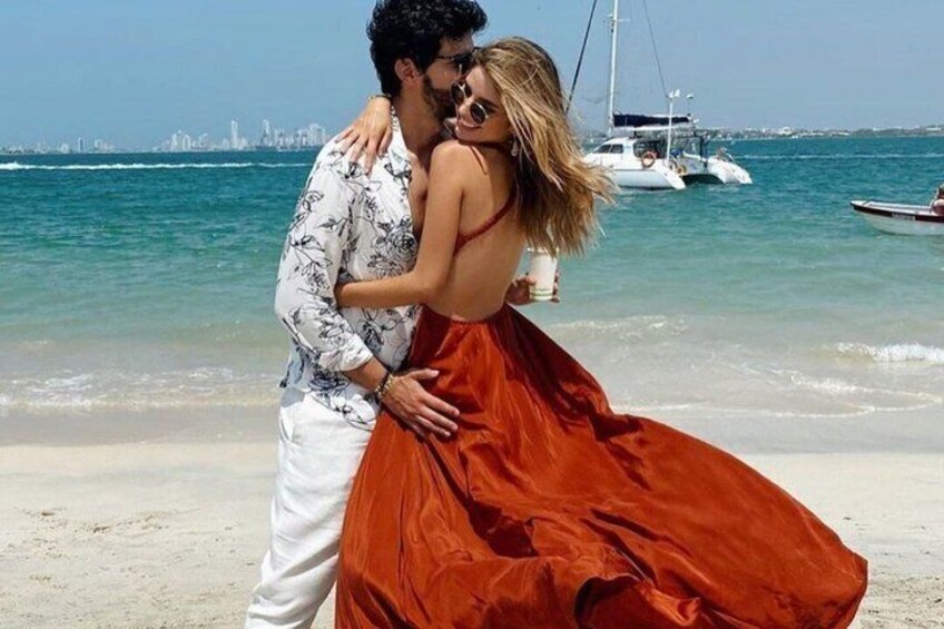 A couple embracing on a beach with boats in the background. 2