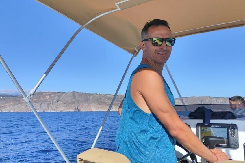 A person on a boat with a clear blue sea and rocky cliffs in the background. 3
