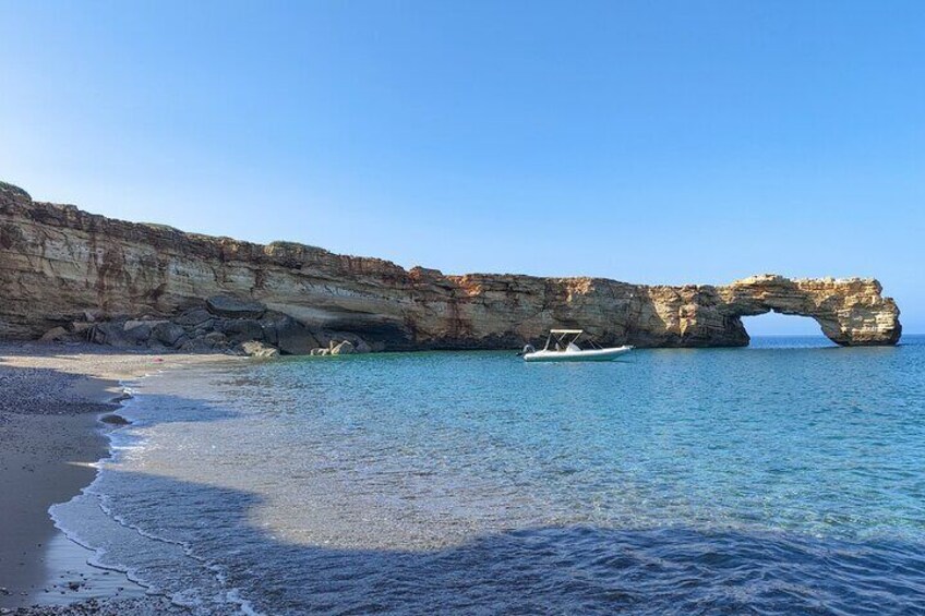 A beach with clear blue waters, a boat, and a natural rock arch formation. 2
