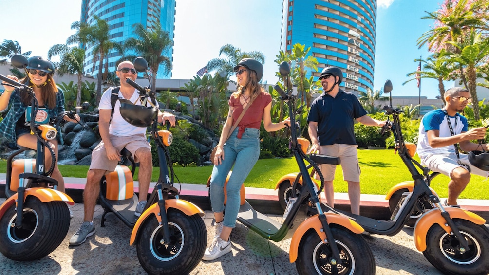 People riding electric scooters in an urban area with tall buildings and palm trees. 1
