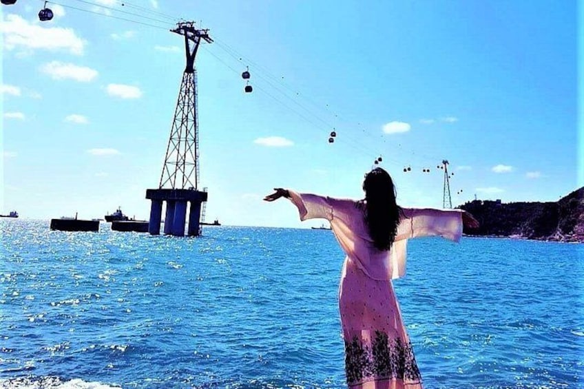 A person standing in the water with arms outstretched, a cable car in the background, and a large structure on the shore. 2