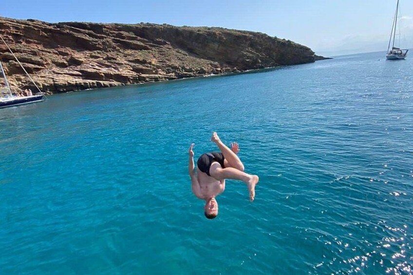 Una persona se sumerge en aguas azules y transparentes, con una costa rocosa y un velero a lo lejos. 2