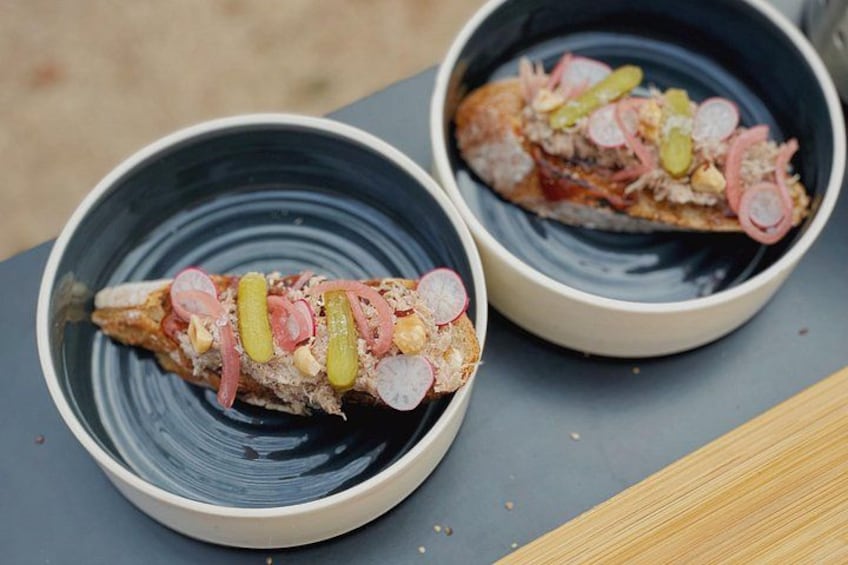 Two bowls of fish topped with pickles and radishes on a table. 2