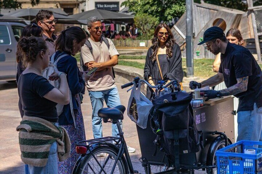 A group of people standing around a bicycle repair station with a cart and a blue basket. 5