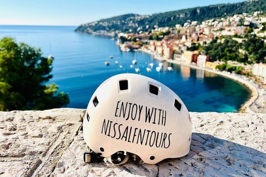 A white helmet with 'ENJOY WITH NISSALFNTOURS' text, a coastal town, and the sea. 2